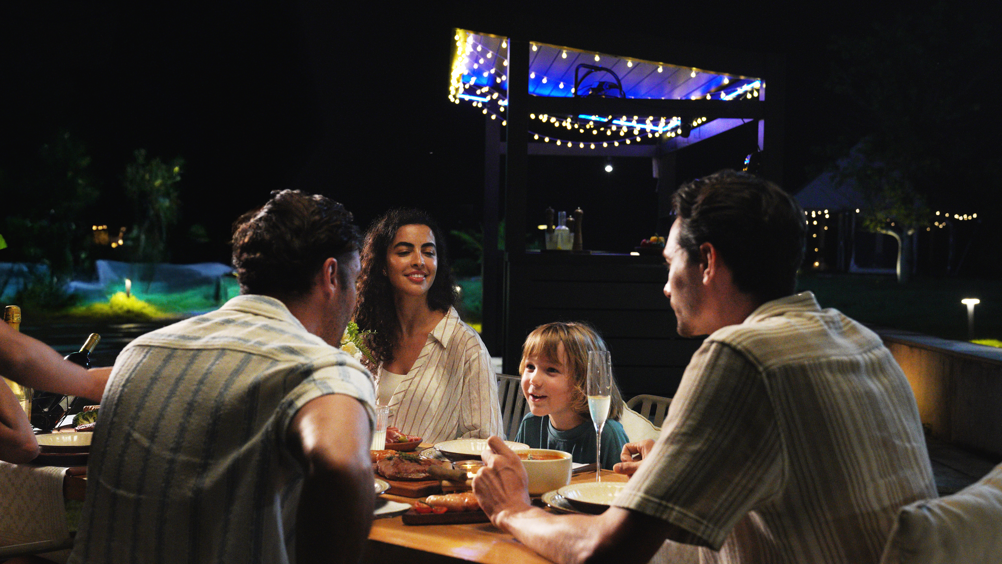 Four people dining outdoors at night under string lights