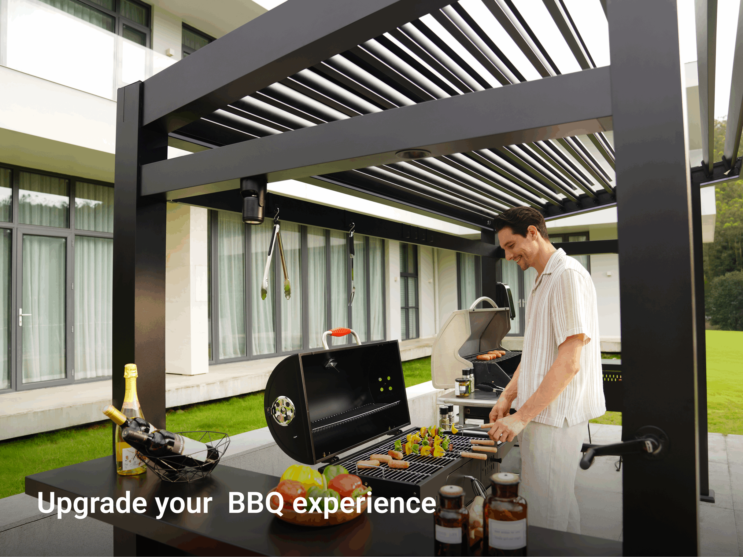 Man grilling on barbecue under black louvered pergola with wine bottles and manicured lawn backdrop.