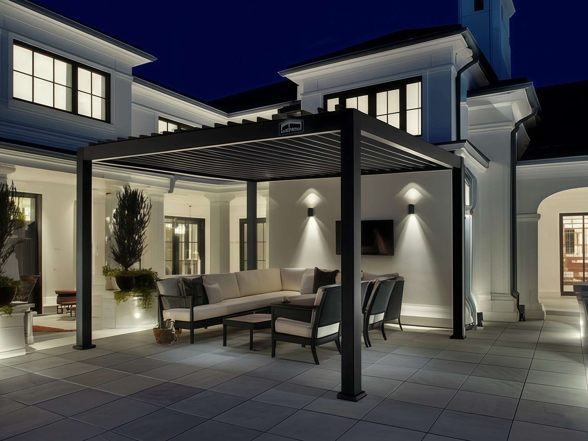 LuxPatio black aluminum louvered pergola with seating and lighting, creating an elegant outdoor living space at night.